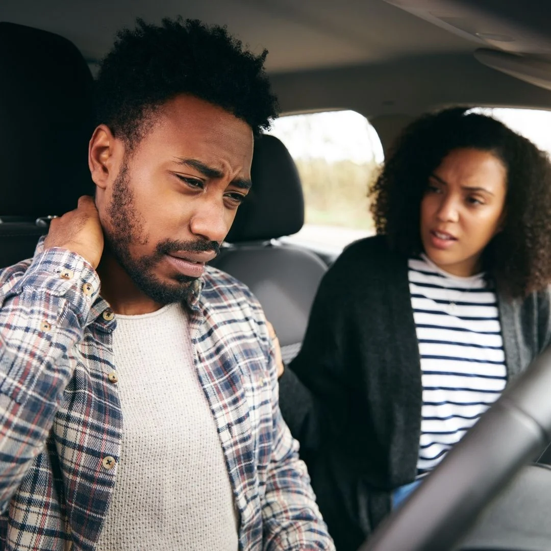 Man holds his neck in passenger seat as woman looks at him in worry after a car accident.
