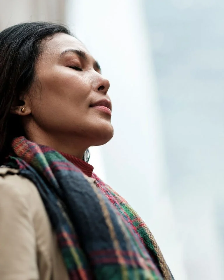 A close-up profile shot of a woman with long dark hair and dark skin, tilt-faced slightly upward with her eyes closed and a calm expression.