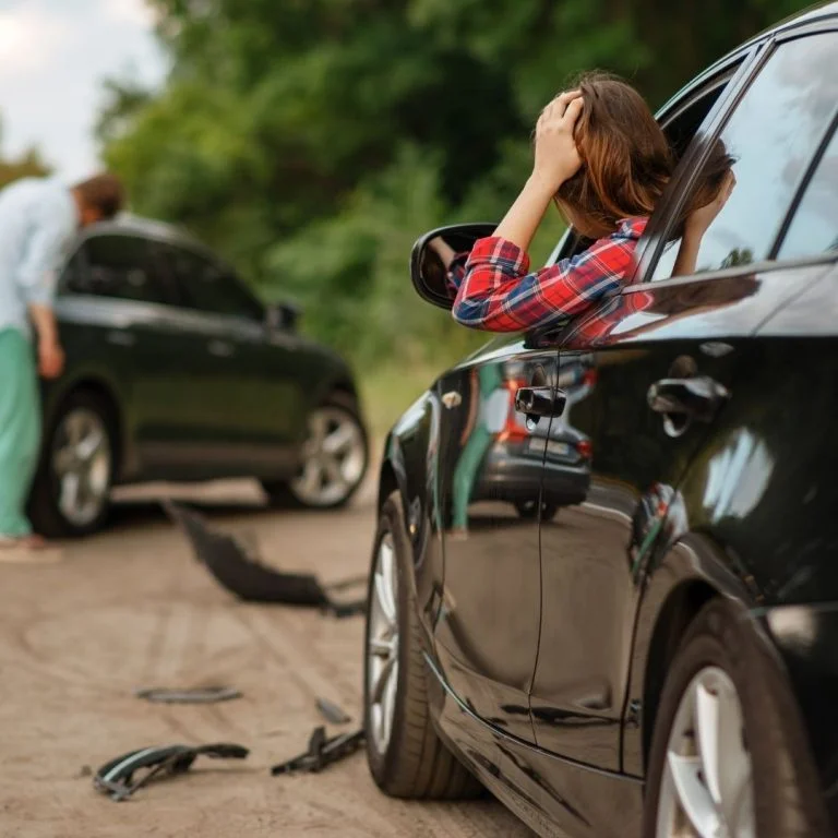 Woman looking at driver side window of car looking at a car accident.