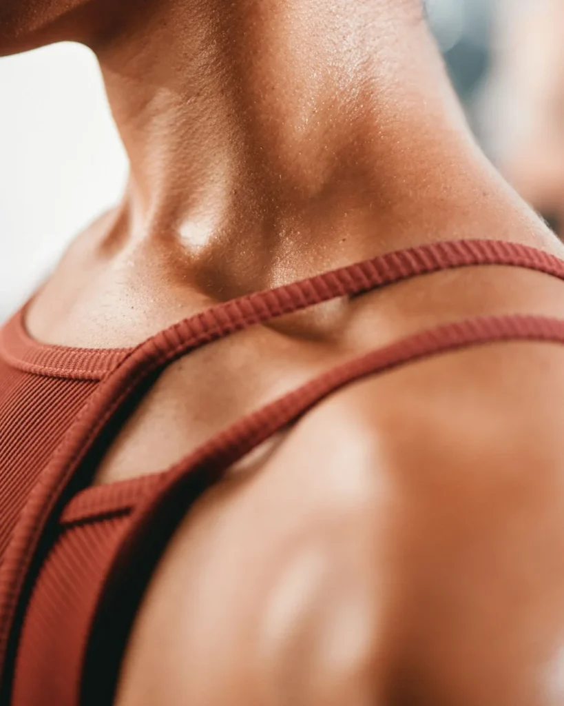 Close-up shot of a person’s neck, collarbone, and shoulder with light sweat after a workout, wearing a reddish-brown athletic top.